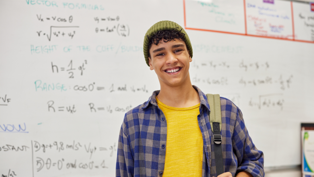 A teen boy stands in front of a whiteboard with mathematical formulas on it.