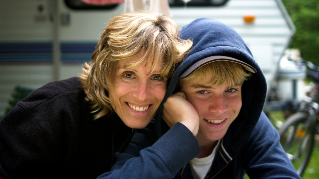 A white mother and teen son pose for a photo with their arms around each other's shoulders.