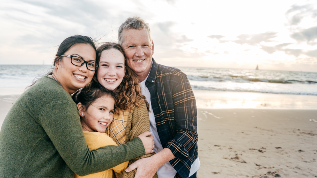A mixed race couple pose for a photo with their two daughters on the beach.